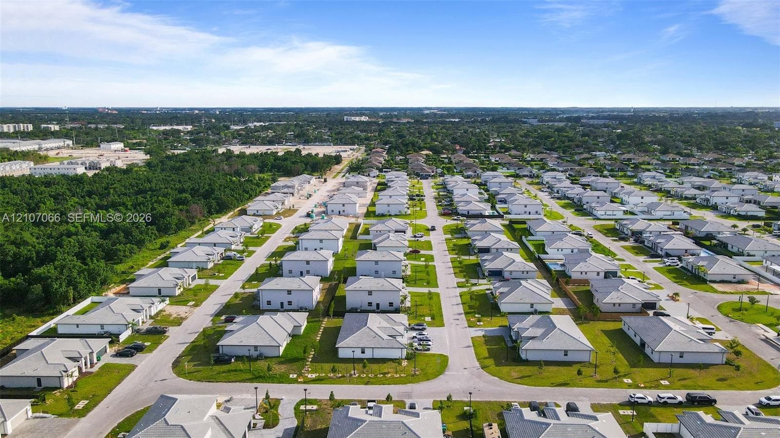 Aerial perspective of a planned residential community featuring paved grid-pattern streets, uniformly spaced detached residences, multi-pitched rooflines, and peripheral woodland buffers
