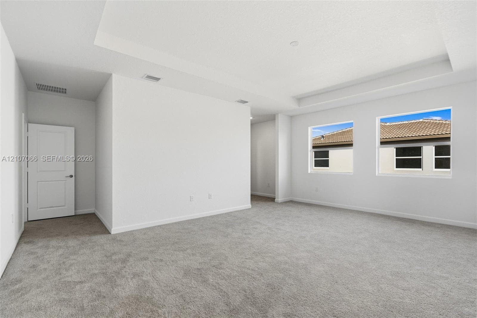 Neutral-toned interior space featuring a recessed tray ceiling, neutral wall-to-wall carpeting, and dual windows with exterior window frames
