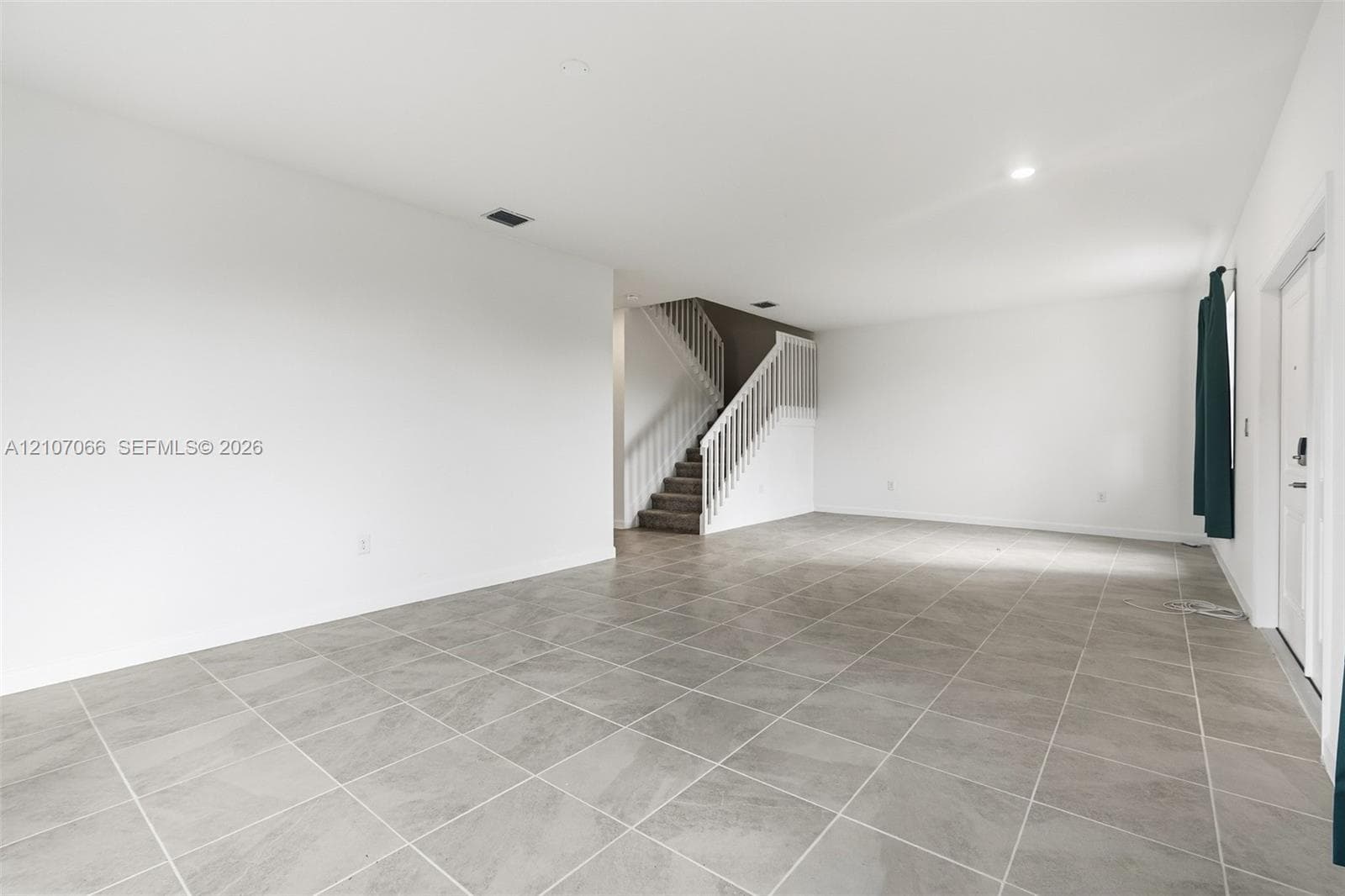 Large-format ceramic tile flooring, neutral wall palette, and white staircase featuring wood-tread steps and white balusters