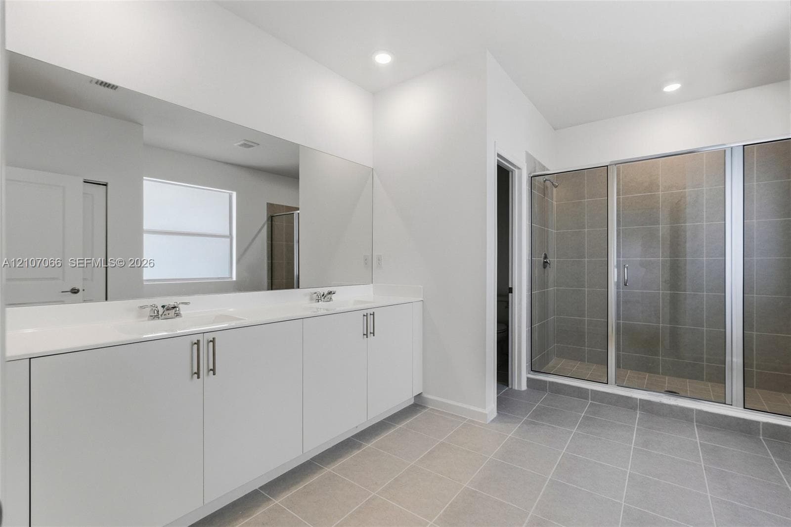 Dual-sink vanity with white cabinetry and solid surface countertop, expansive wall-to-wall mirror, and walk-in shower with tiled surround and metal-framed glass enclosure