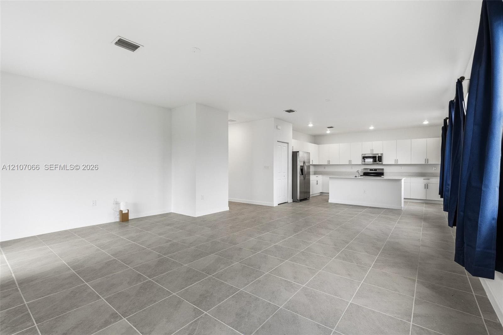 Open-concept interior featuring large-format tile flooring, white cabinetry, a center island with a stone-finish countertop, and recessed ceiling lighting