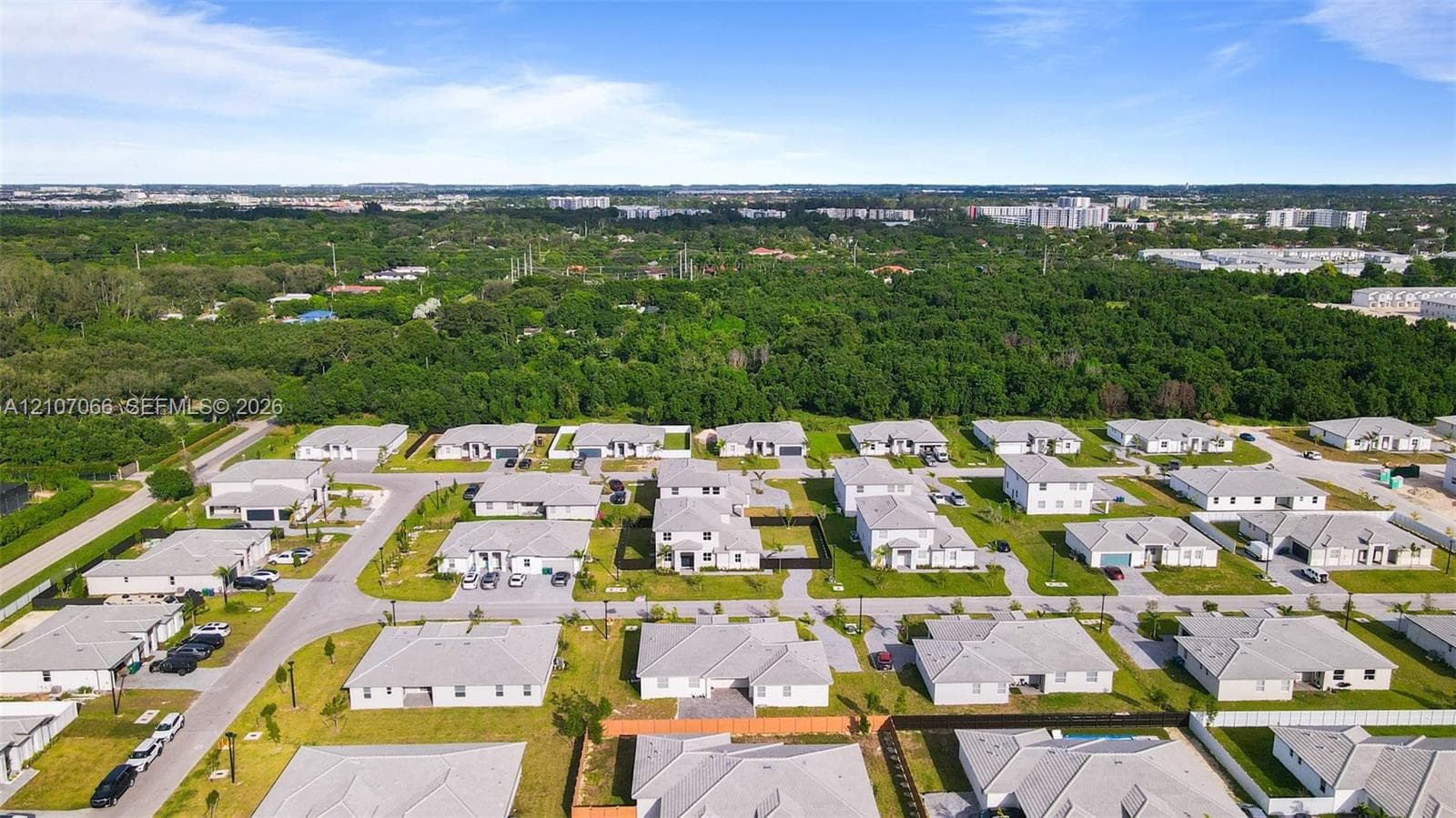 Aerial perspective of a planned residential development featuring uniform structural designs, paved street infrastructure, integrated sidewalks, and expansive green space buffers
