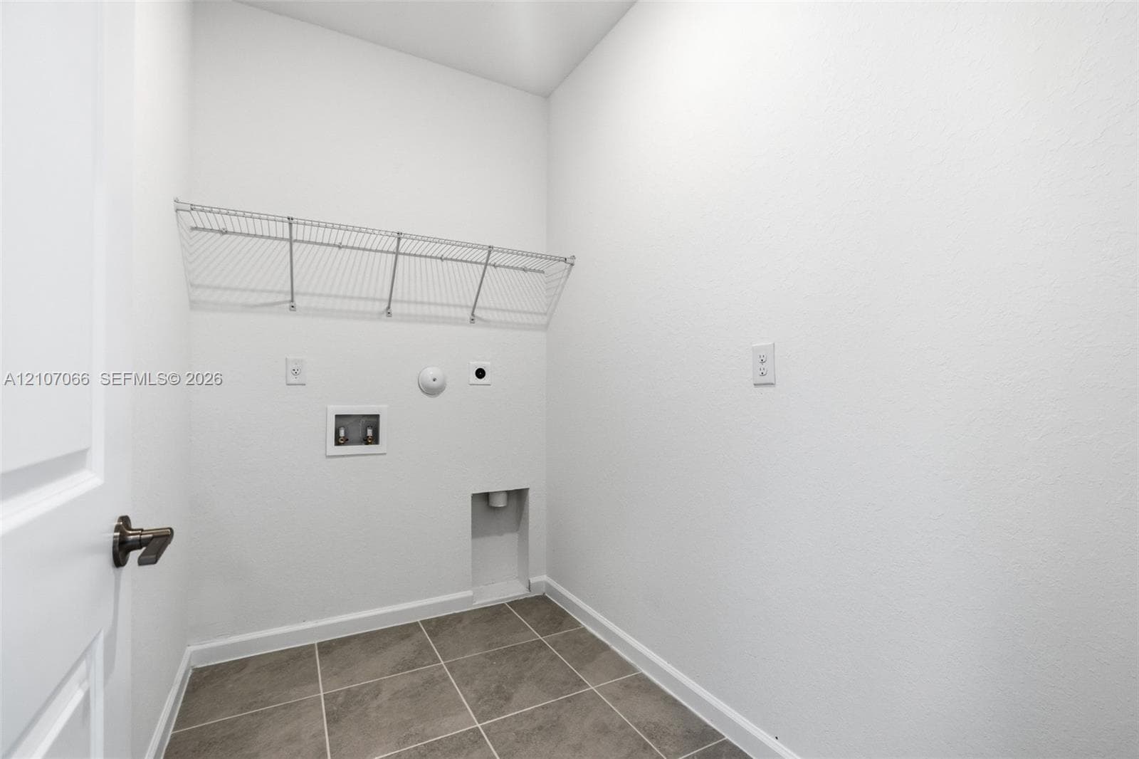 Utility area featuring neutral tile flooring, wall-mounted wire shelving, and dedicated hookups for laundry appliances