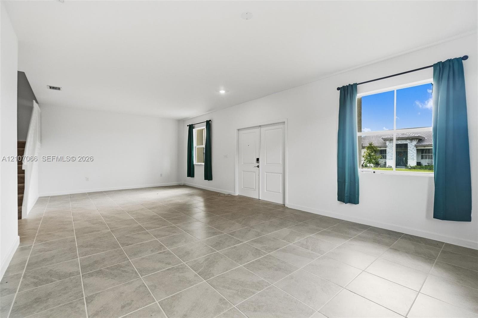 Open-concept room featuring large-format stone-tile flooring, recessed lighting, double-entry doors, and multiple windows with fixed curtain rods