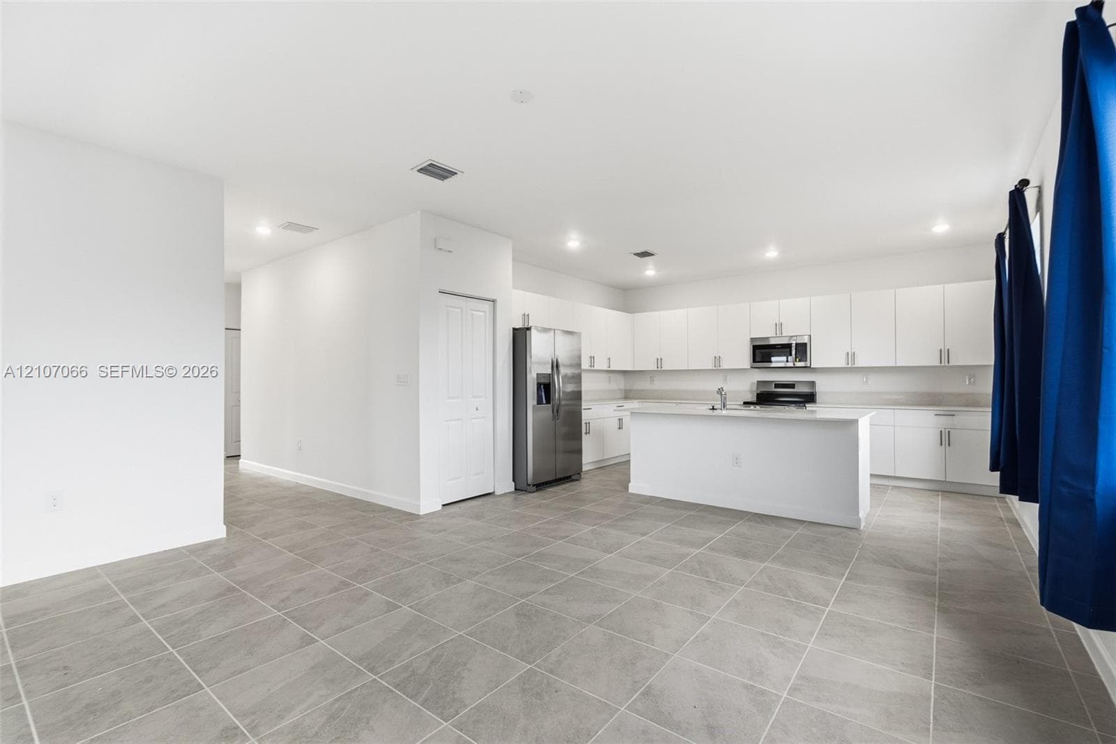 Kitchen featuring white flat-panel cabinetry, a central island, stainless steel appliances, and tile flooring