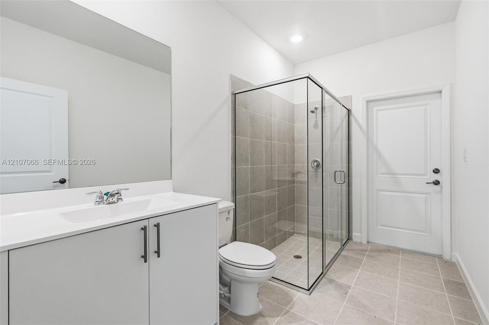 Bathroom featuring a vanity with a solid-surface countertop, a walk-in shower with glass enclosure and tile surround, a wall-mounted mirror, and tile flooring