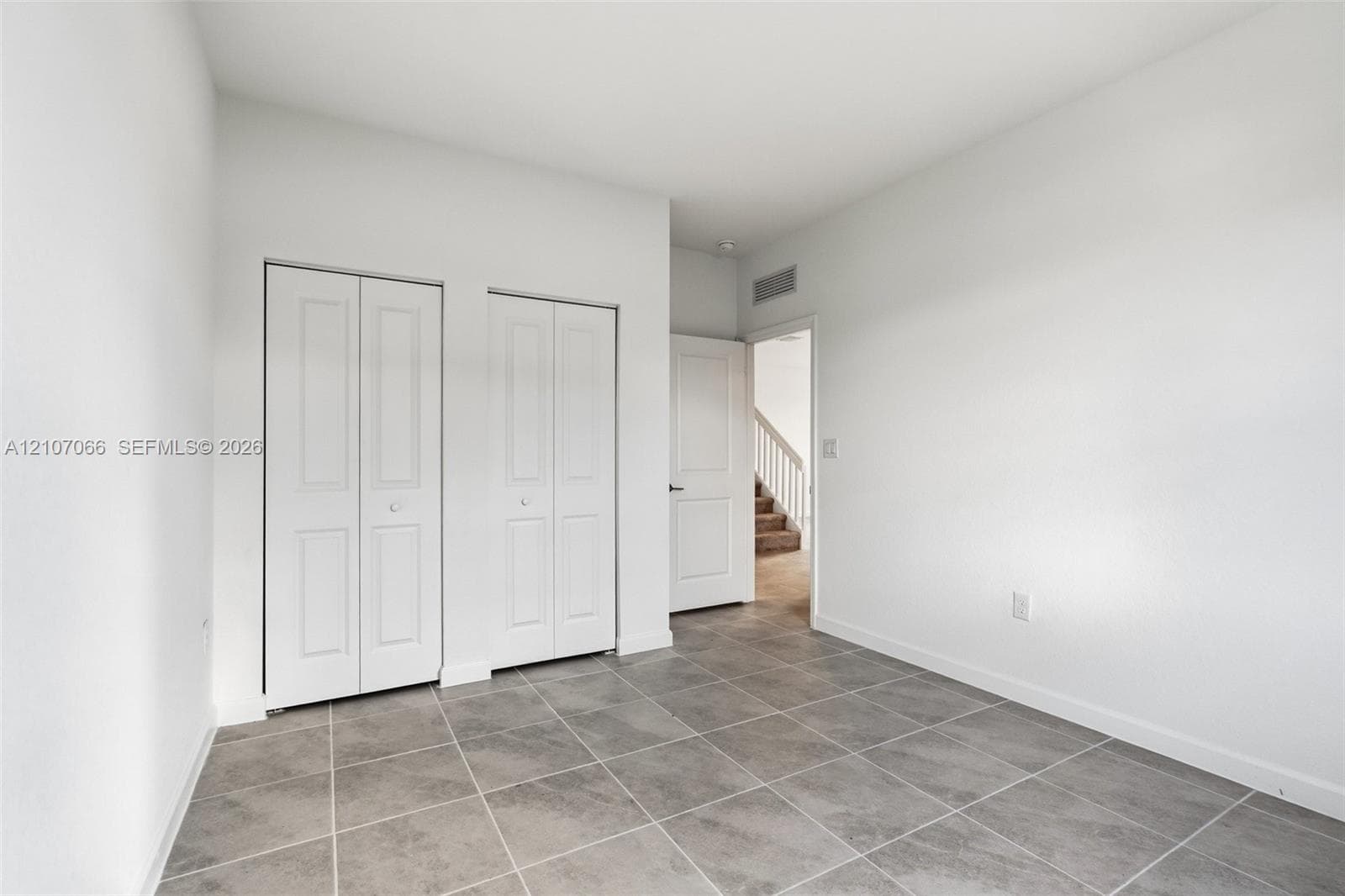 Neutral interior featuring ceramic tile flooring, two white bifold closet doors, and crisp white wall finishes