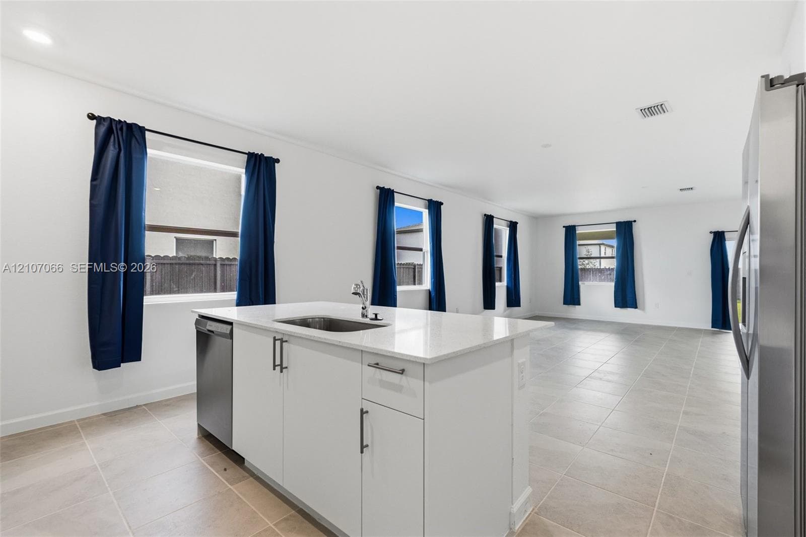 Kitchen island featuring a white countertop, under-mount stainless steel sink, and built-in dishwasher, complemented by large-format tile flooring and multiple windows