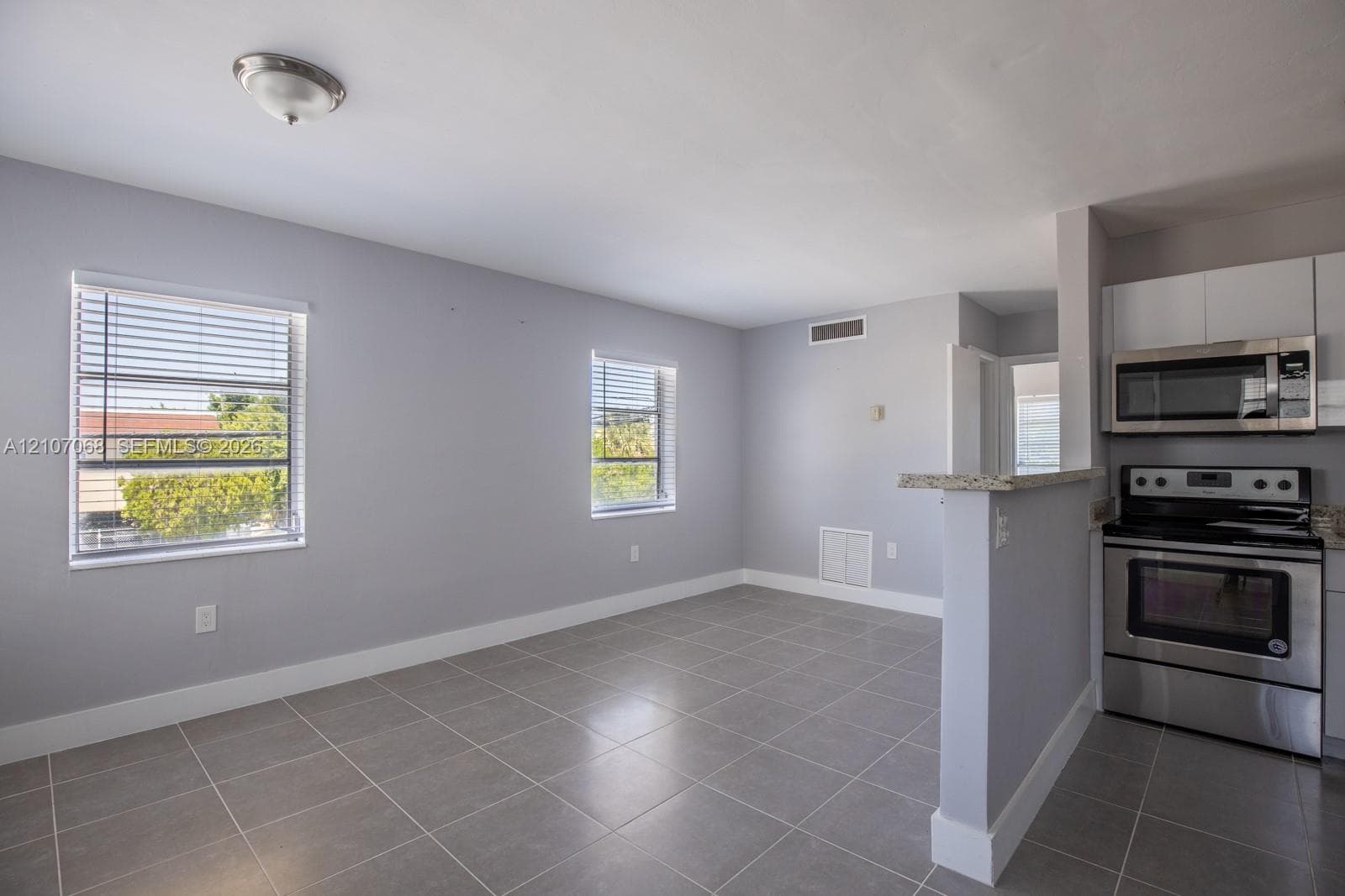 Neutral-toned interior featuring large-format tile flooring, oversized windows with horizontal blinds, stainless steel kitchen appliances, and stone-finish countertops