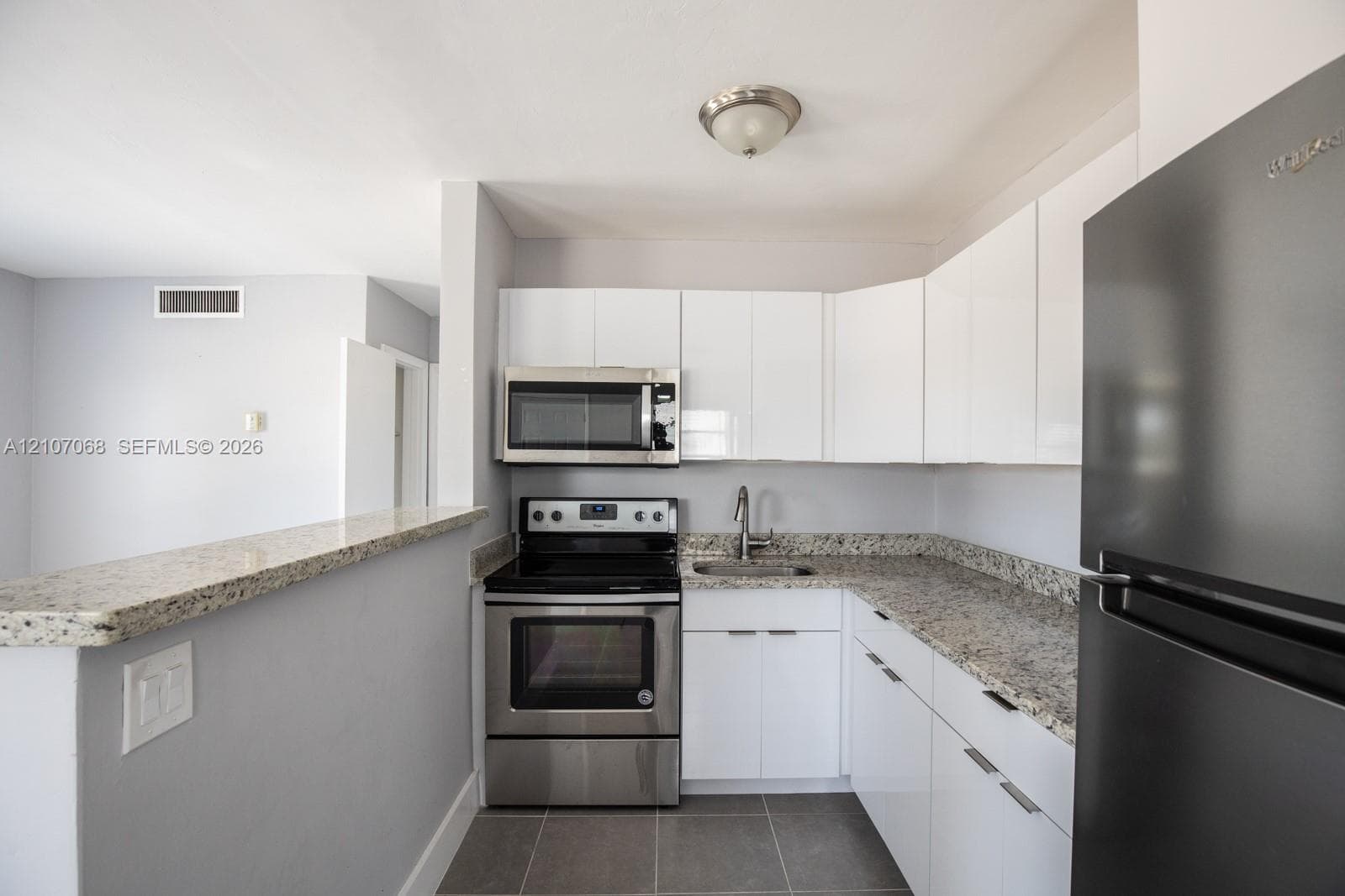 Kitchen featuring white gloss cabinetry, stone-finish countertops, stainless steel appliances, and large-format tile flooring