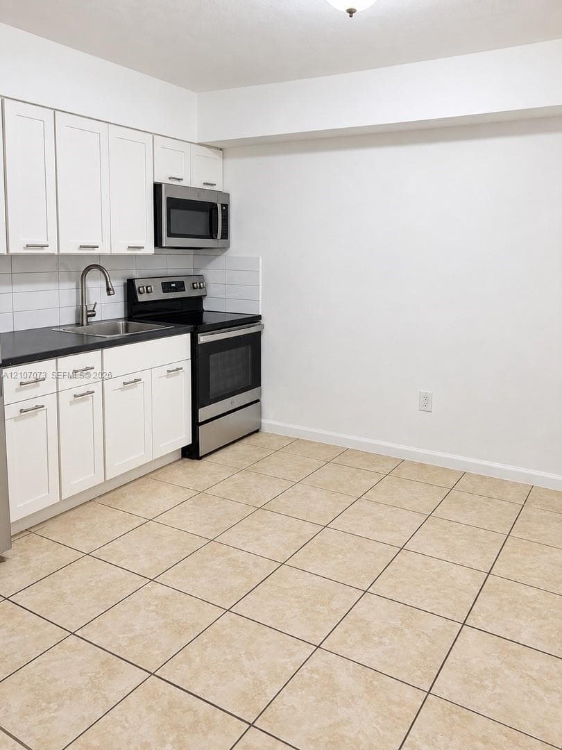Kitchen featuring white shaker-style cabinetry, dark countertops, stainless steel appliances, white subway tile backsplash, and ceramic tile flooring