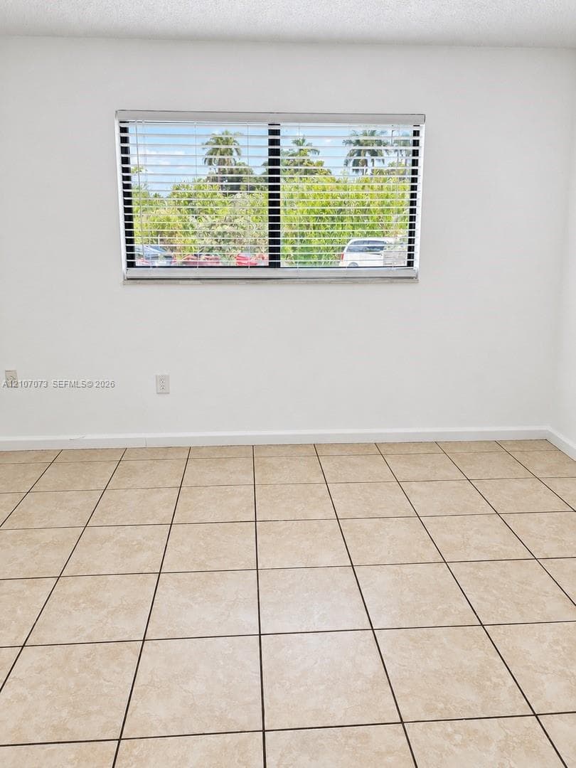 Neutral-toned ceramic tile flooring, horizontal window blinds, and a window with exterior palm tree scenery