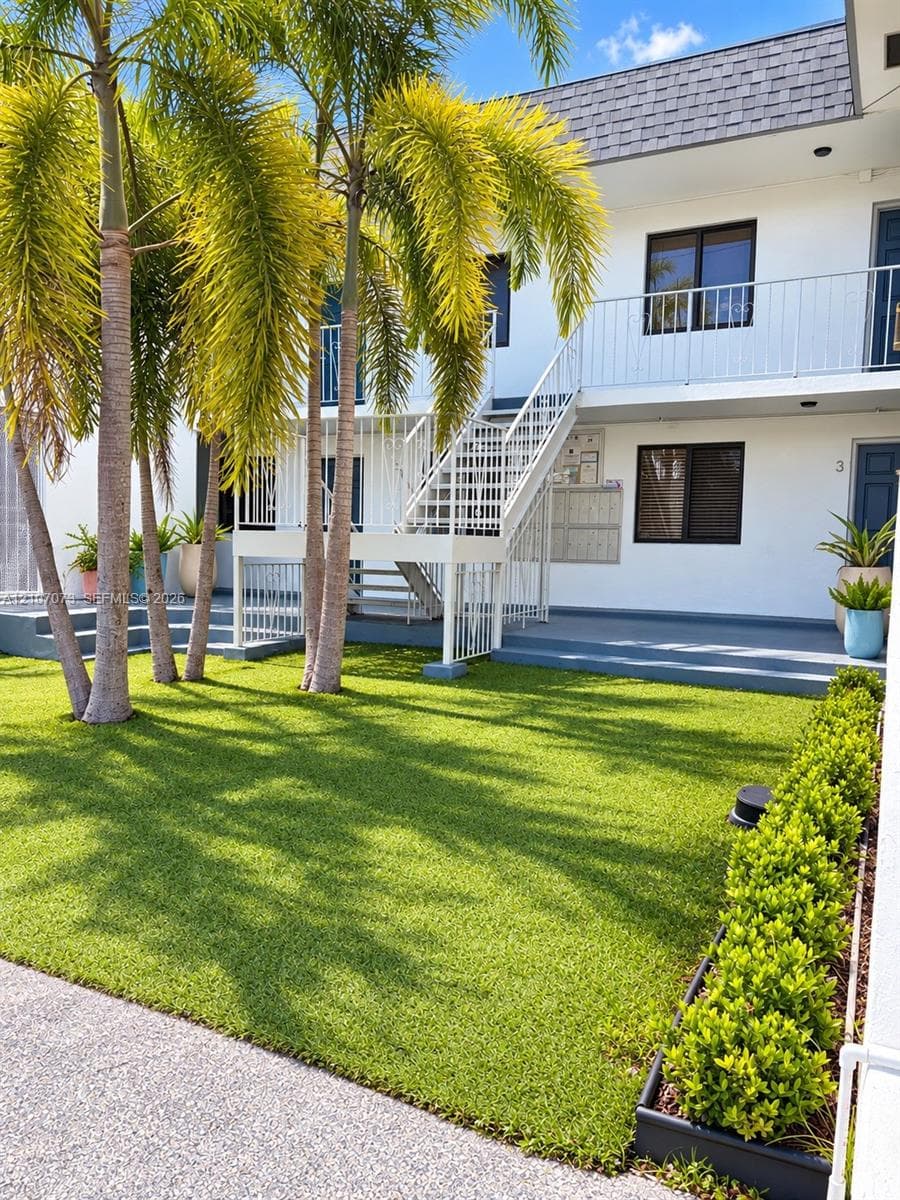 Manicured lawn featuring mature palm trees, white metal exterior staircase, and a concrete patio