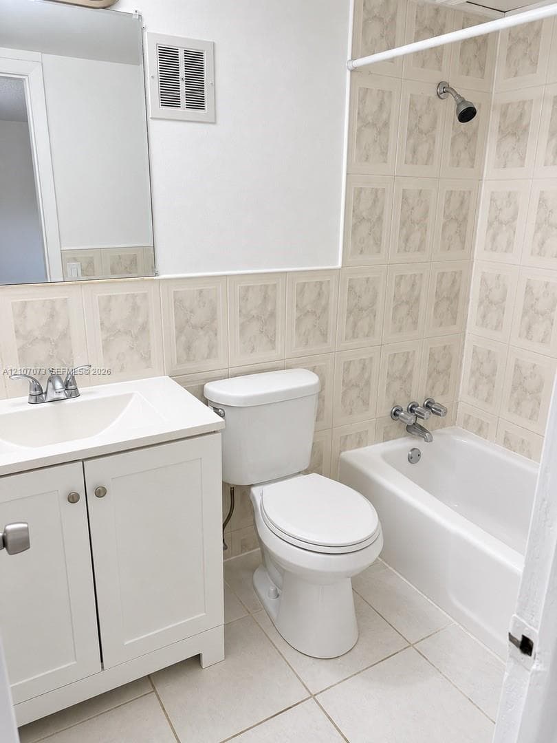 Bathroom featuring a white vanity cabinet with a composite countertop, wall-mounted mirror, ceramic tile wainscoting, and a porcelain-enamel bathtub with a wall-mounted showerhead