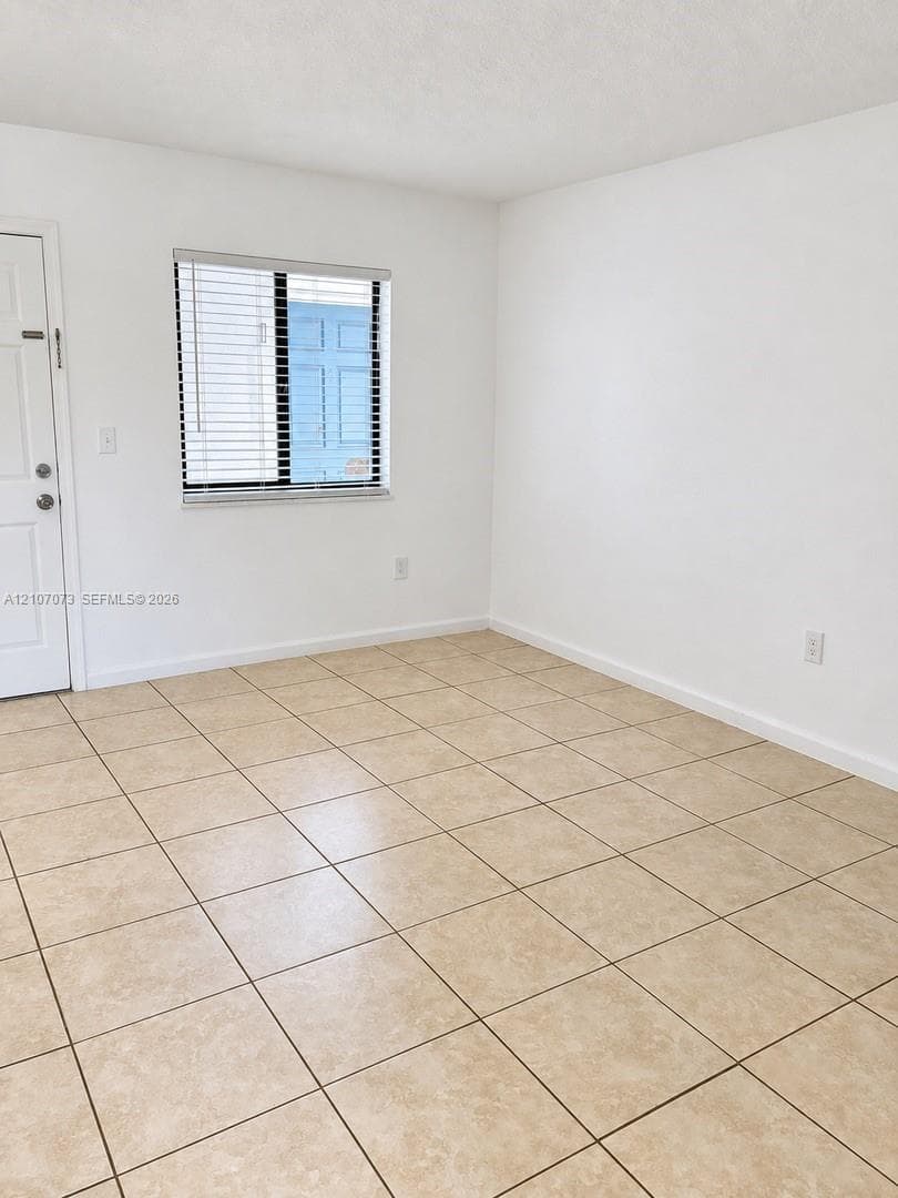 Neutral interior space featuring ceramic tile flooring, solid-surface walls, and a single-hung window with horizontal blinds