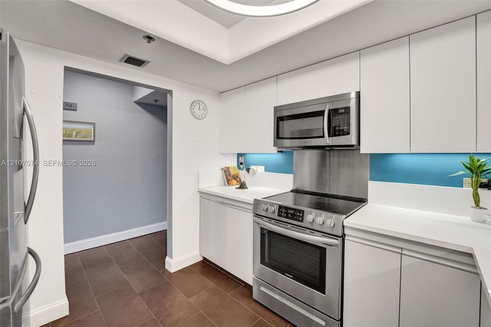Kitchen featuring white flat-panel cabinetry, stainless steel appliance suite, solid-surface countertops, tile flooring, and recessed ceiling lighting