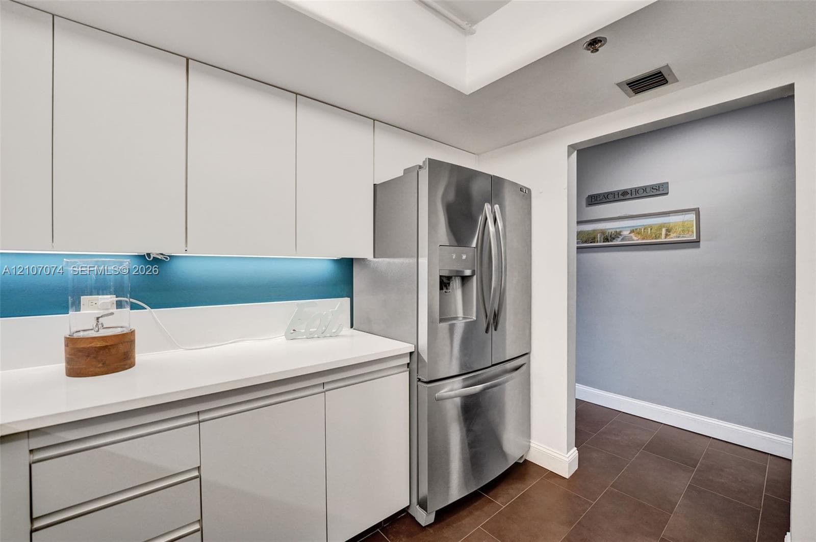 Flat-panel cabinetry, white solid-surface countertops, blue-tinted integrated backsplash, and stainless steel French-door refrigerator