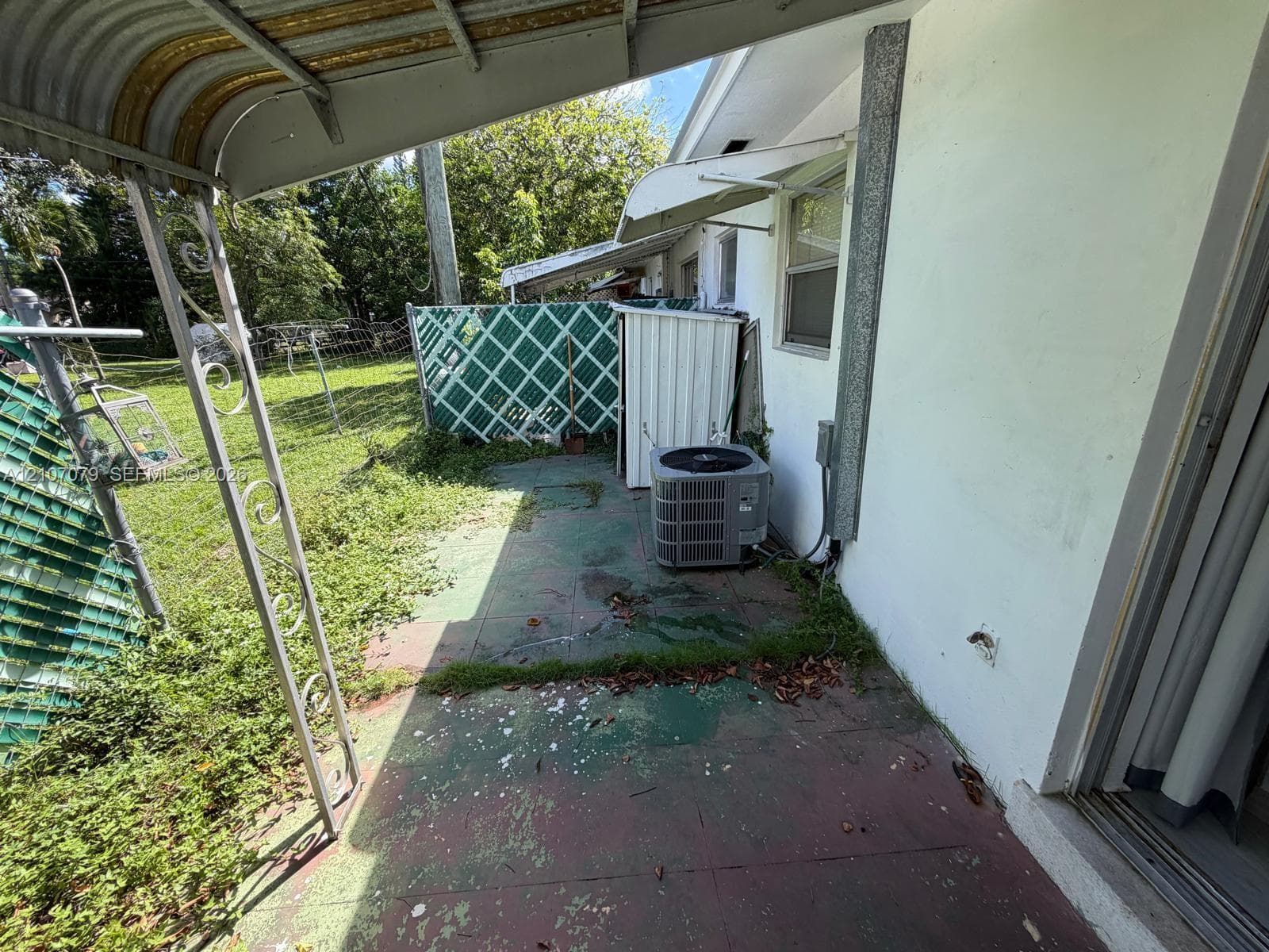 Covered concrete patio featuring metal structural supports, lattice fencing, and exterior climate control unit