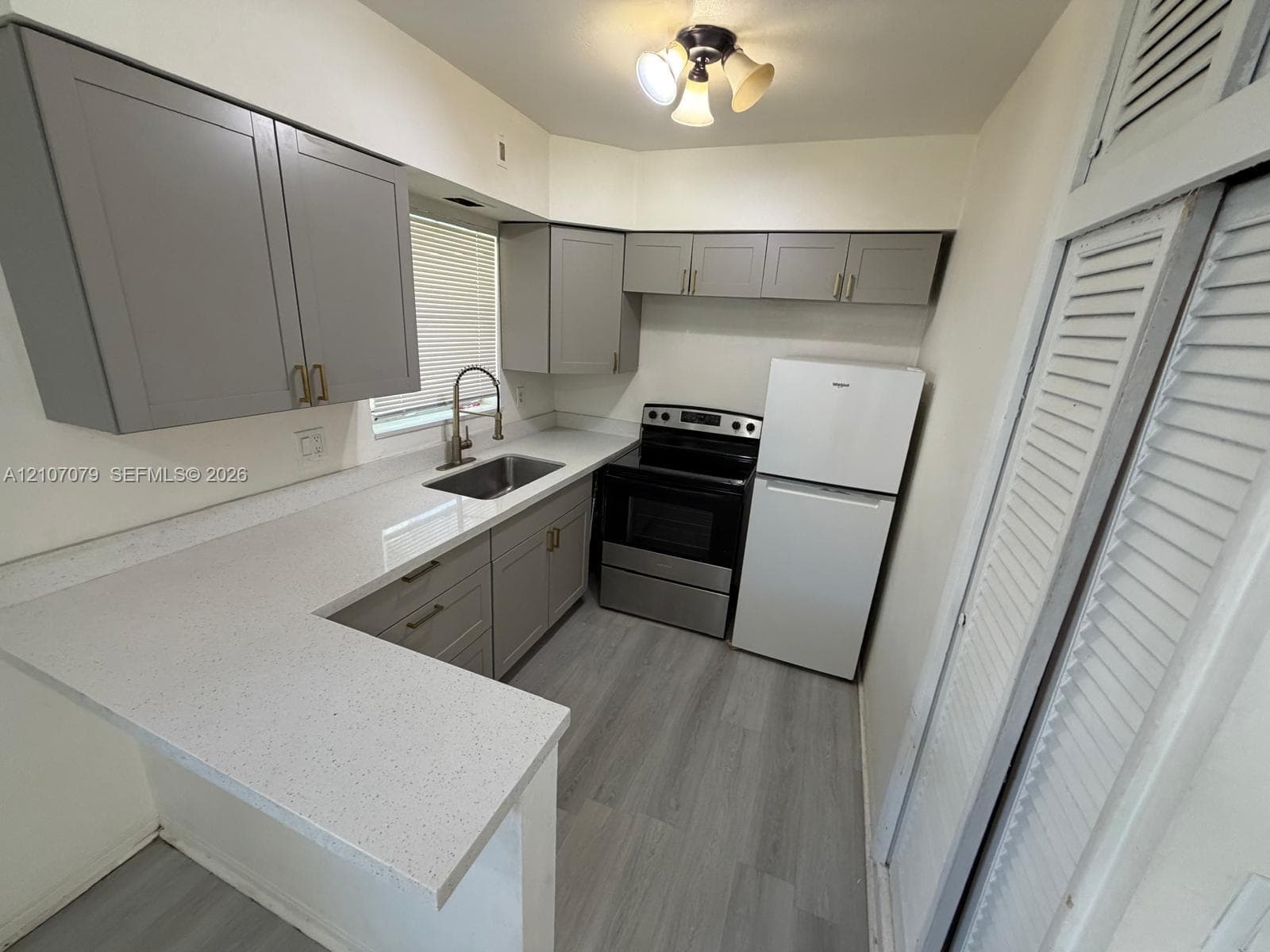 Kitchen featuring gray shaker-style cabinetry, solid-surface countertops, wood-finish flooring, undermount stainless steel sink, and built-in closet with louvered doors