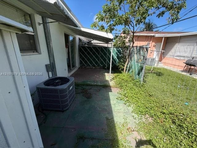 Concrete patio area featuring a fixed metal awning, exterior HVAC unit, and chain-link perimeter fencing