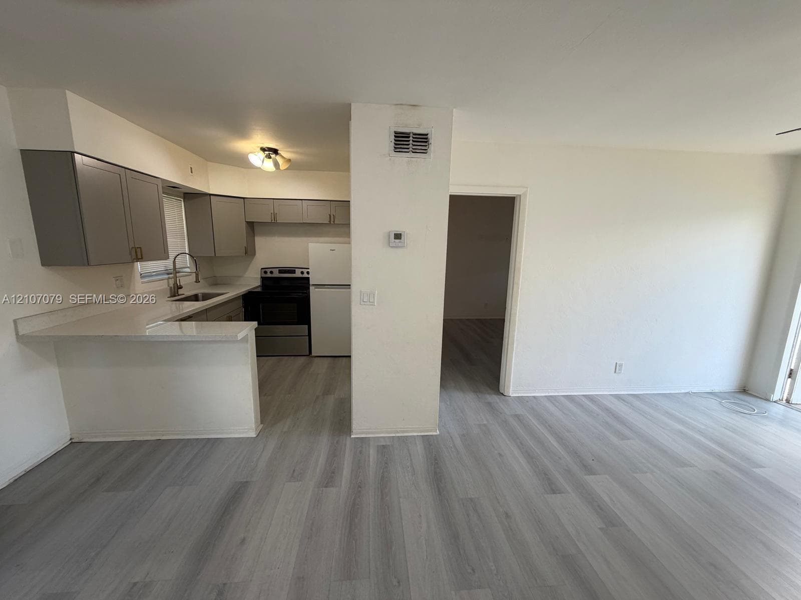 Kitchen featuring gray shaker-style cabinetry, solid-surface countertops, wood-finish flooring, and a stainless steel sink with gooseneck faucet