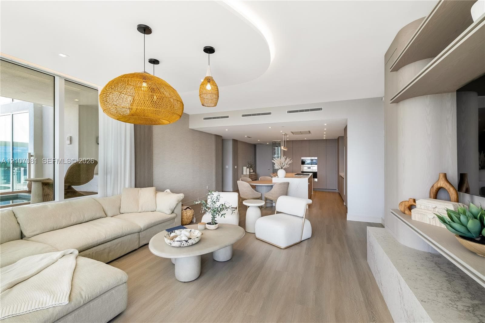Open-concept living space featuring wood-finish flooring, recessed cove lighting, a custom built-in media console with stone-finish surfaces, and large-format sliding glass doors