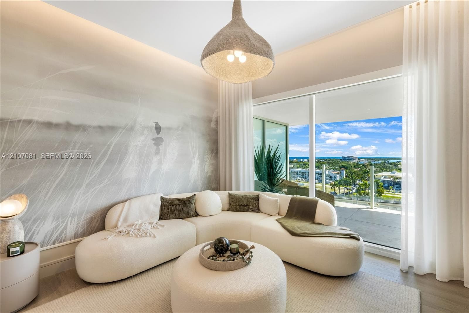 Floor-to-ceiling sliding glass door, spacious balcony with glass railing, large custom pendant lighting, recessed cove lighting, and neutral-toned wall mural