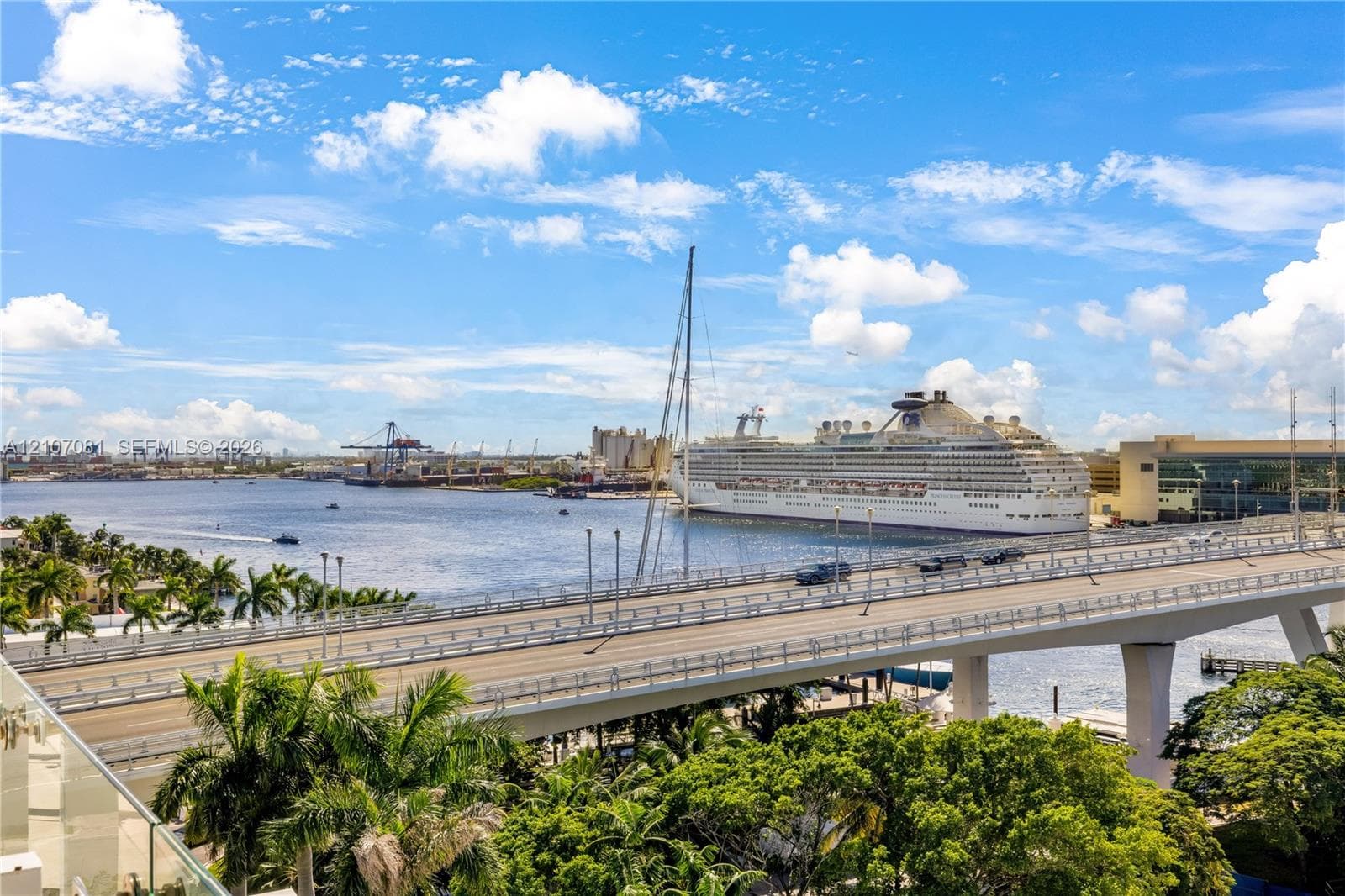 Elevated harbor and waterway scenery featuring a multi-lane bridge, industrial maritime activity, and mature palm trees