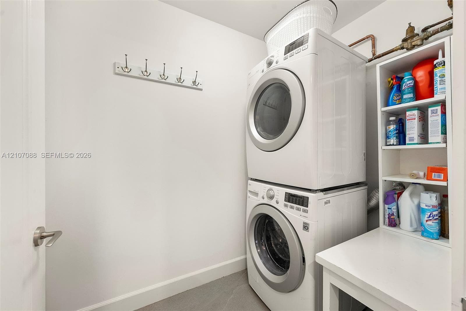 Laundry area featuring a stacked washer and dryer, built-in open shelving, and a wall-mounted hook rack