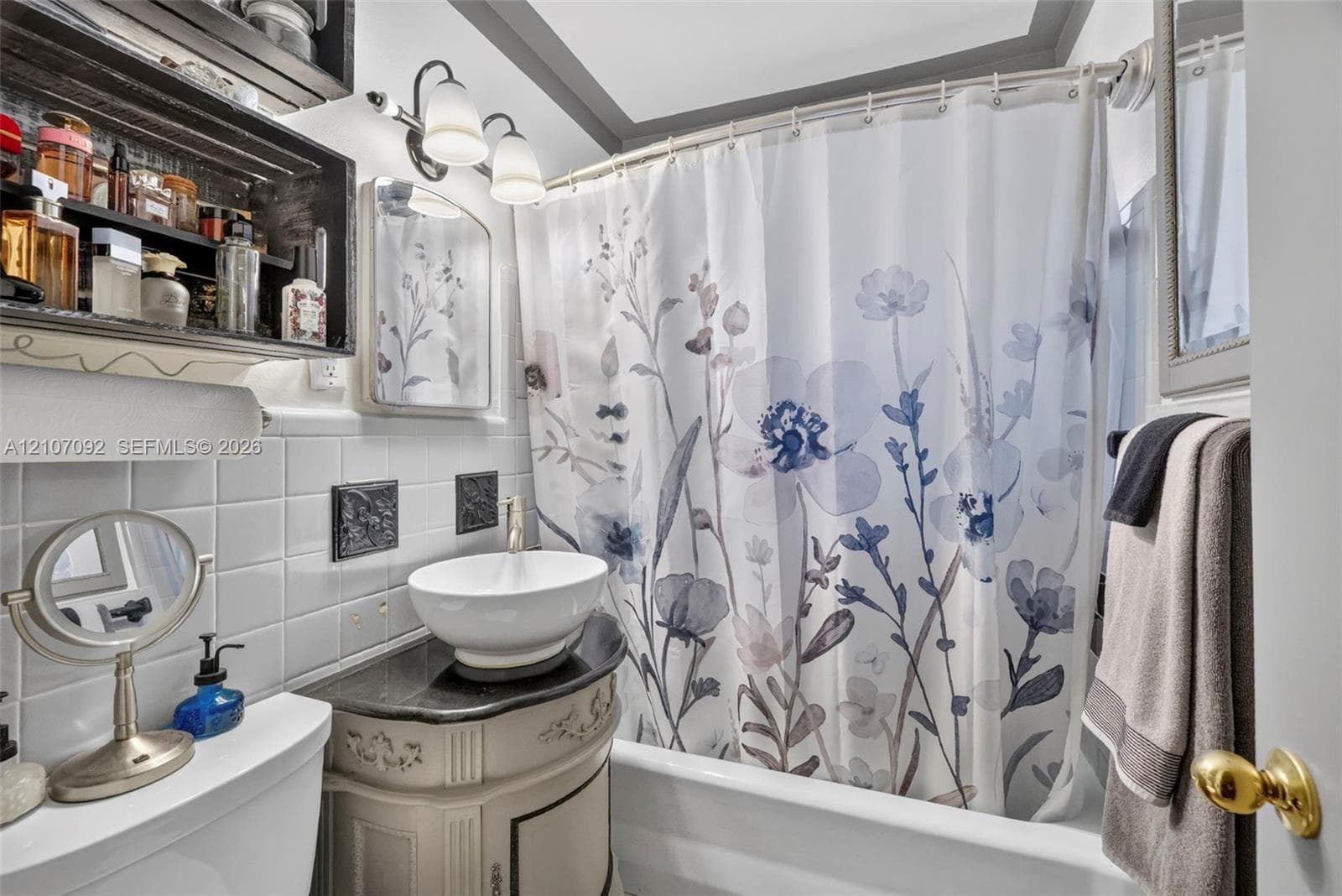 Bathroom featuring a vessel sink with a dark stone-finish countertop, white square wall tile, built-in shelving, and dual-bulb vanity lighting