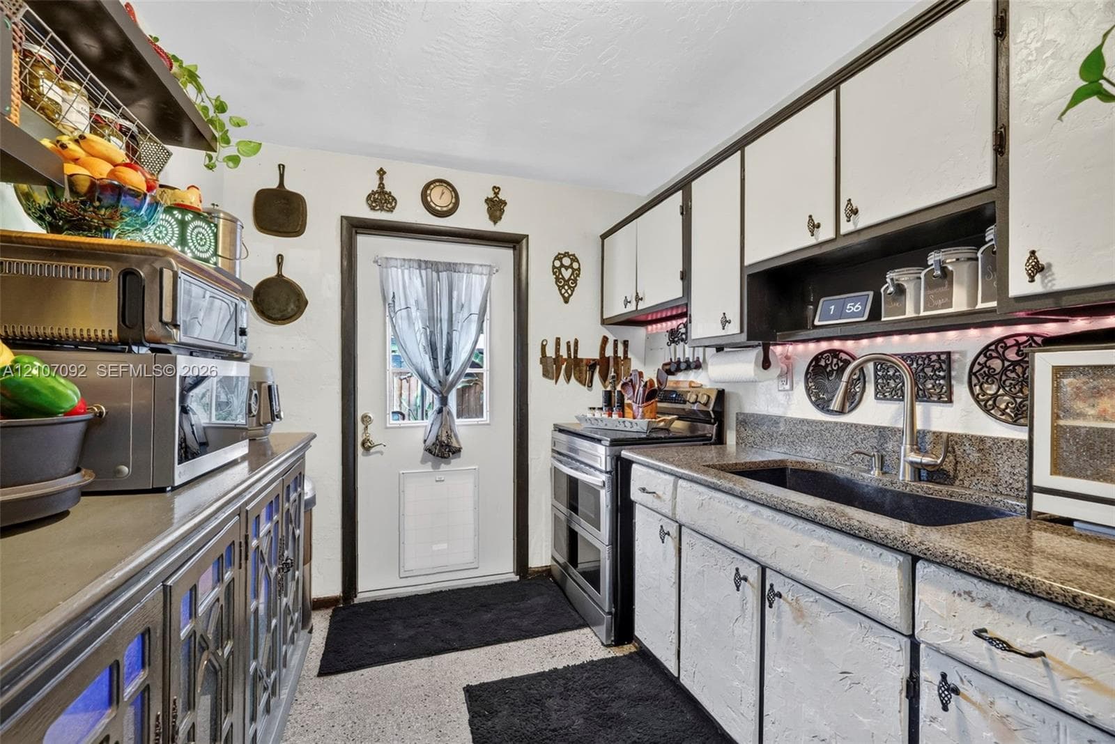 Kitchen featuring stone-finish countertops, an undermount sink with a high-arch faucet, custom cabinetry with glass-panel detailing, and an exterior entry door