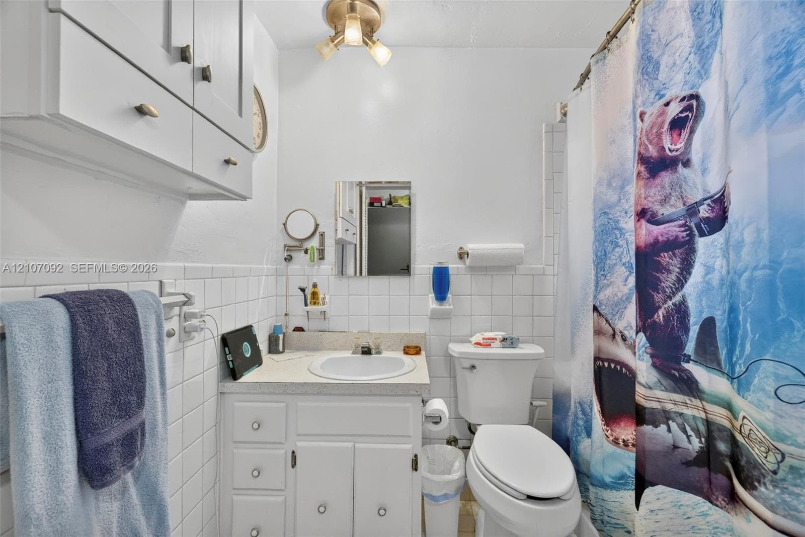 Bathroom featuring white ceramic wall tile, a built-in vanity with integrated basin, upper wall-mounted cabinetry, and a three-light fixture