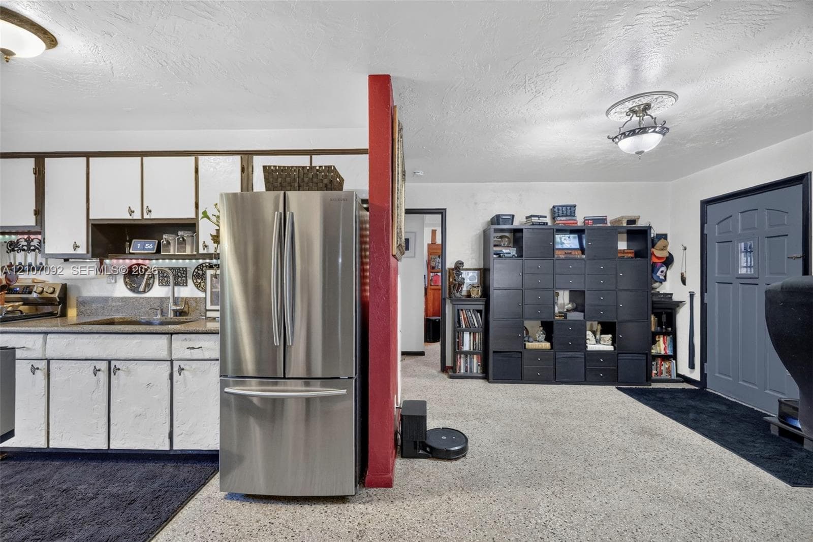 Kitchen featuring white cabinetry, solid surface countertops, and a stainless steel French-door refrigerator, complemented by ceiling-mounted light fixtures and an exterior entry door