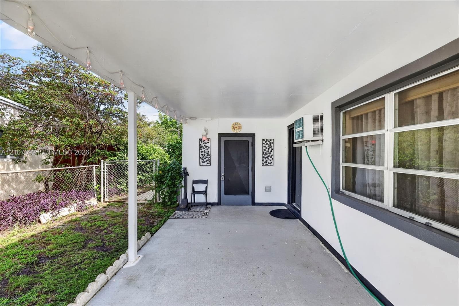 Covered concrete patio featuring a clean white exterior finish, multi-pane windows with dark trim, and a secure entryway