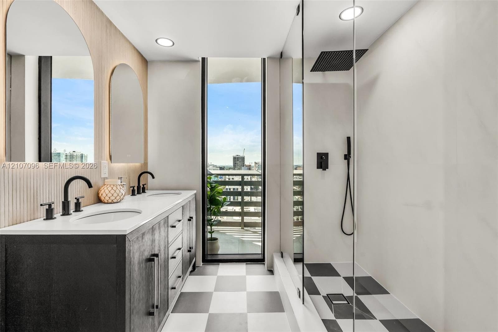 Double vanity with a white solid-surface countertop, dark cabinetry, arched wall mirrors, matte black fixtures, and a glass-enclosed shower featuring a rain-style showerhead and checkerboard tile flooring