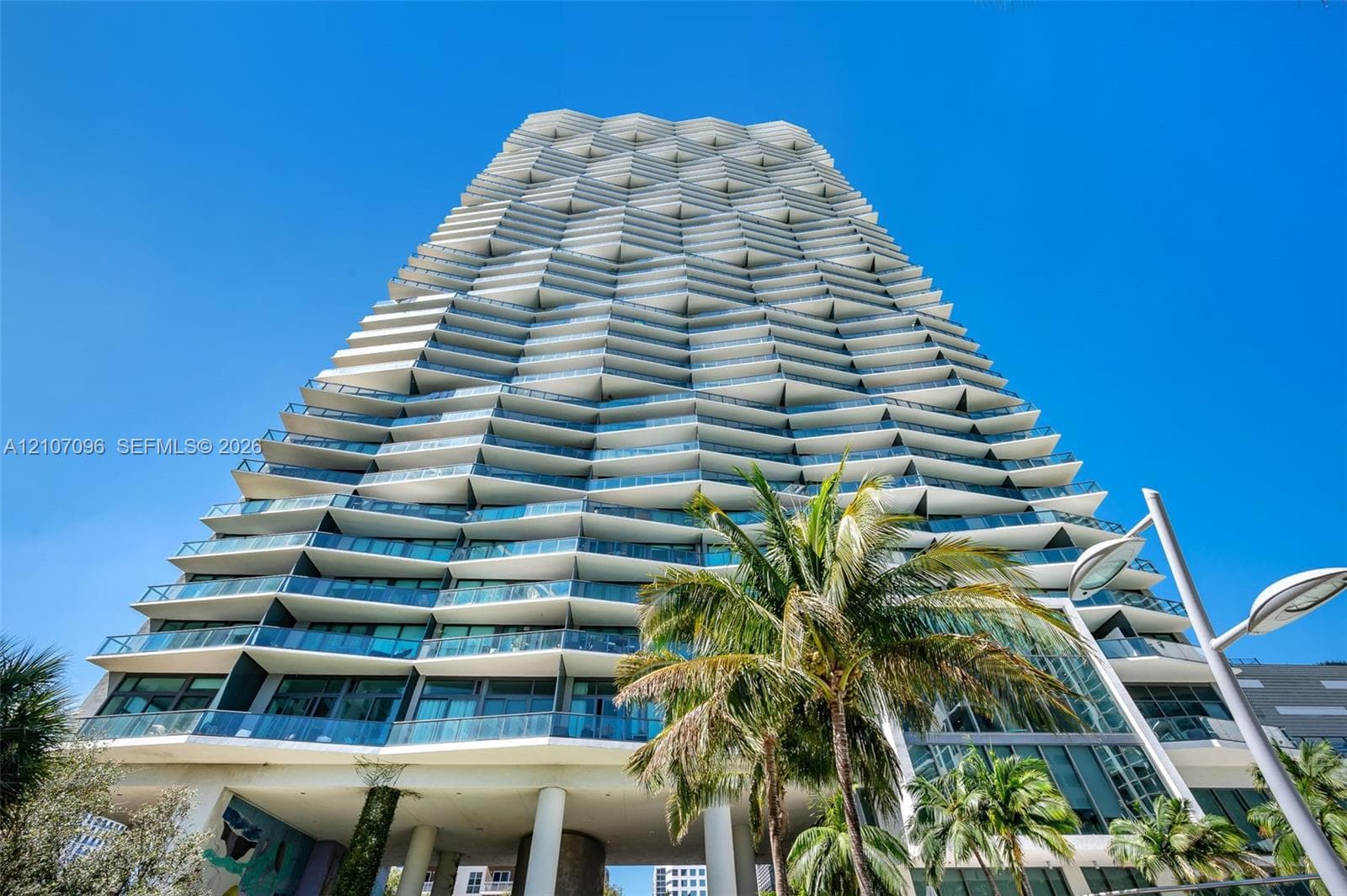 High-rise building featuring a geometric facade with stacked, angular cantilevered balconies, glass-paneled railings, and floor-to-ceiling windows