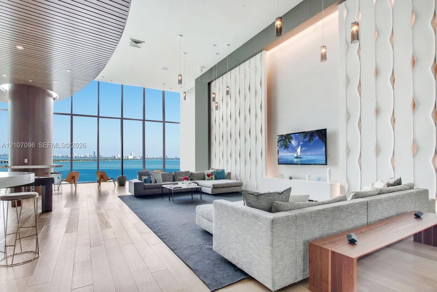 Expansive floor-to-ceiling windows featuring panoramic water scenery, wood-finish flooring, curved ceiling detail, and floor-to-ceiling textured accent wall with integrated pendant lighting