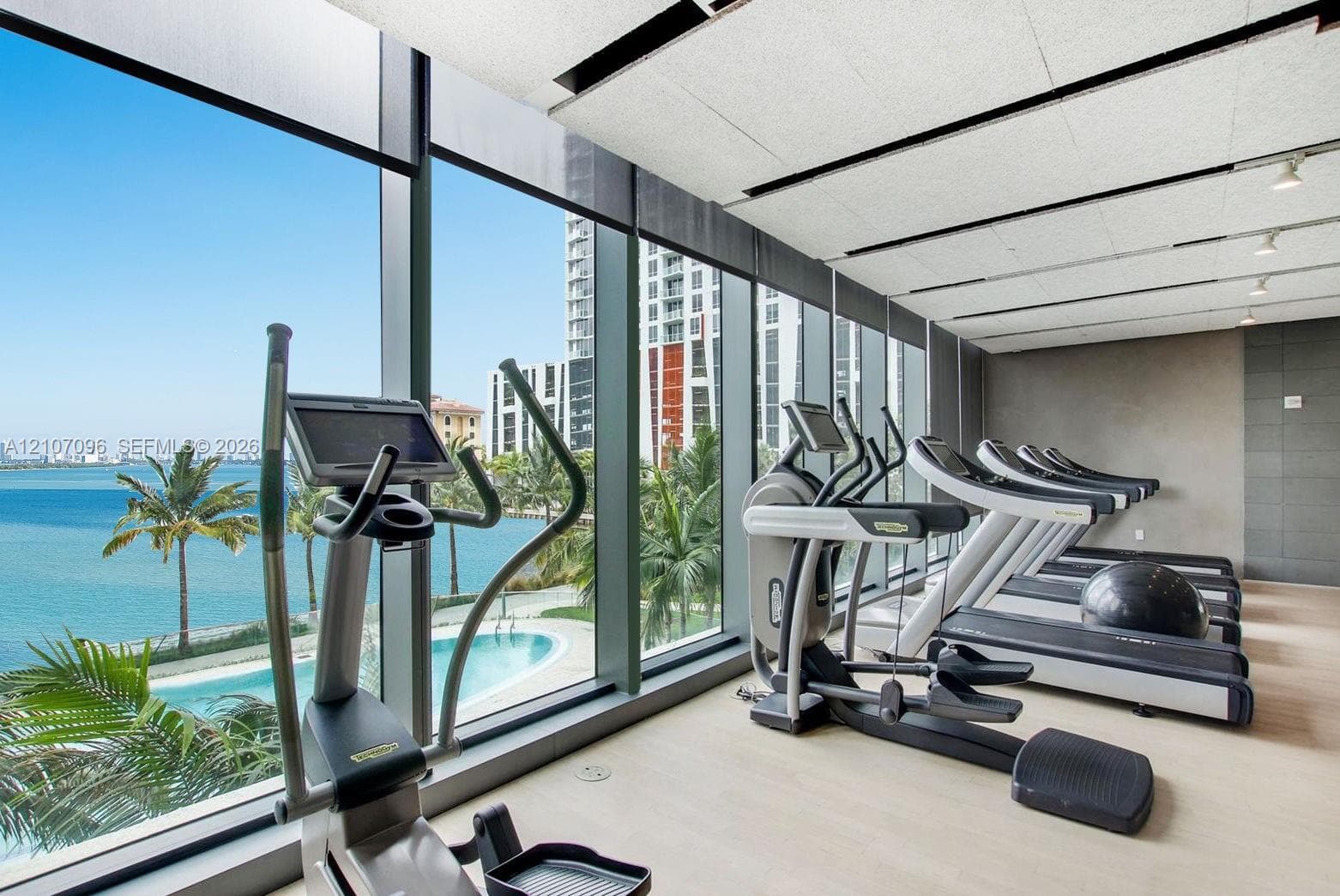 Fitness facility featuring floor-to-ceiling windows, water-facing exterior exposure, neutral stone-finish wall accents, and recessed track lighting