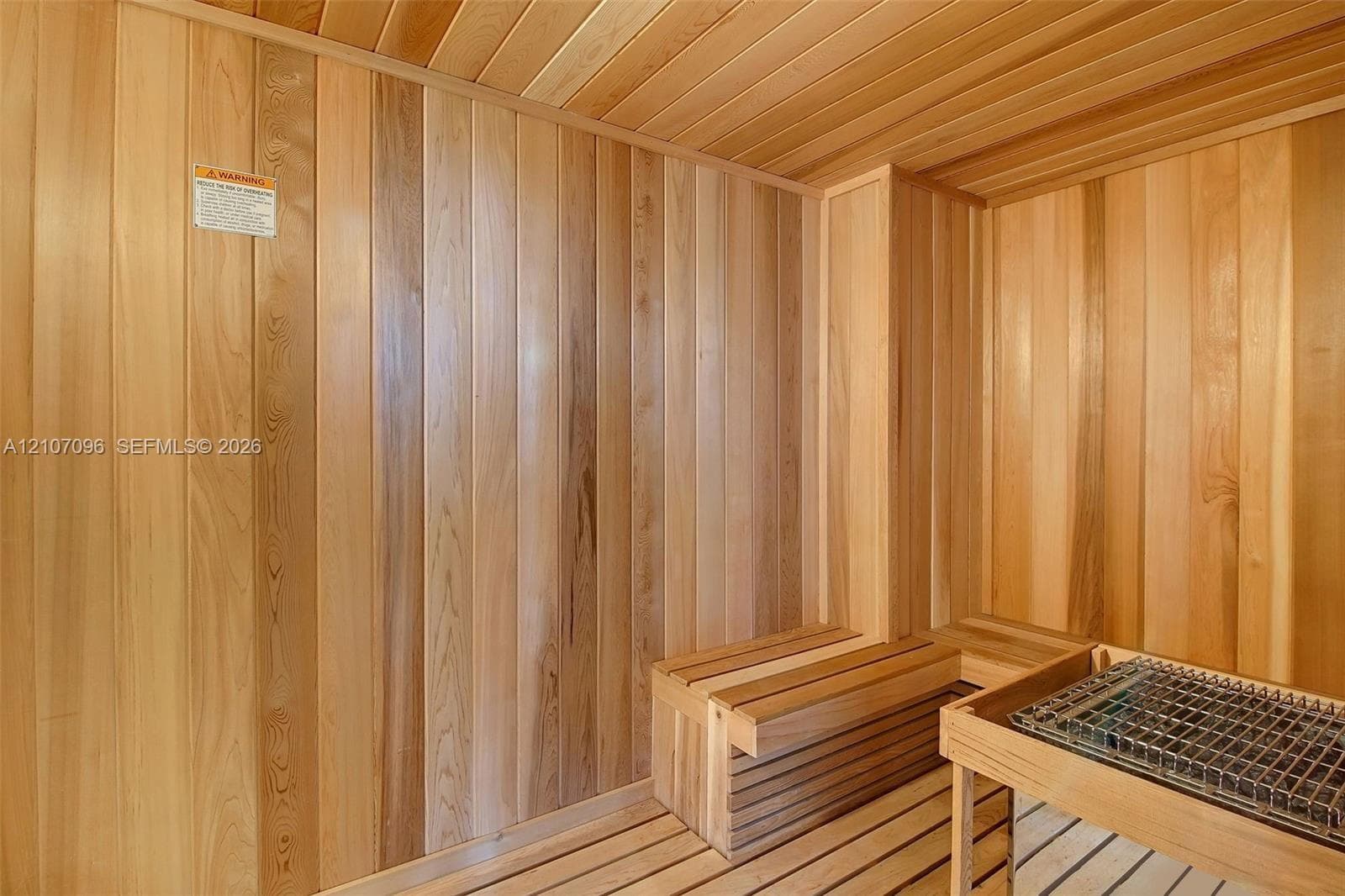 Sauna room featuring tongue-and-groove wood paneling, wood-plank flooring, and built-in tiered bench seating with an integrated heating unit and protective metal guard