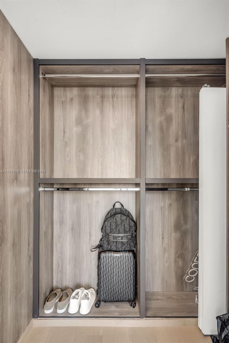 Built-in closet featuring wood-finish laminate cabinetry, metal frame detailing, and dual-level metal hanging rods