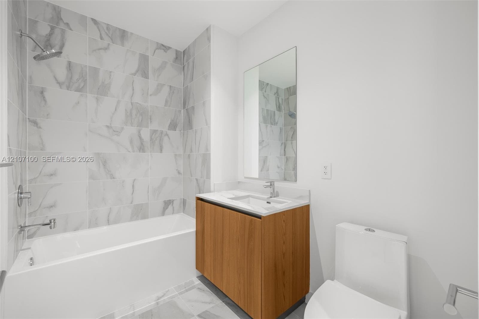 Kitchen featuring white handle-less cabinetry, wood-finish upper cabinets, integrated wine refrigerator, and stone-finish backsplash, with a restroom highlighting a floating wood-finish vanity and stone-tile flooring