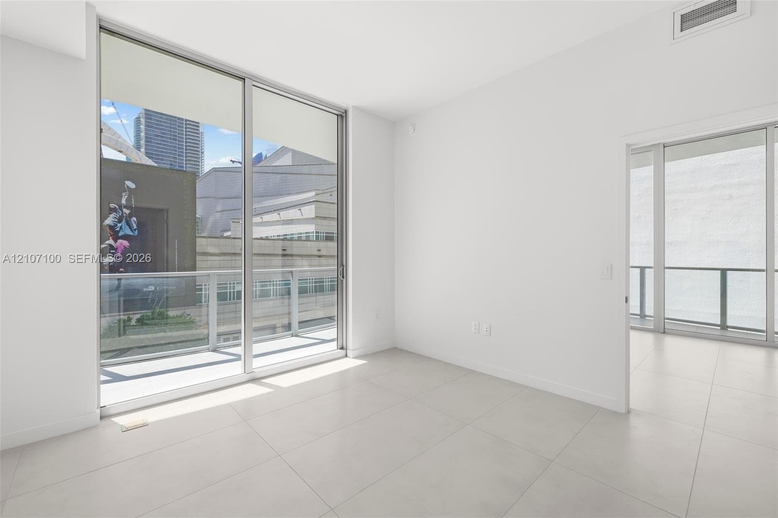 Floor-to-ceiling sliding glass doors, large format neutral floor tiling, and a private balcony featuring metal railing