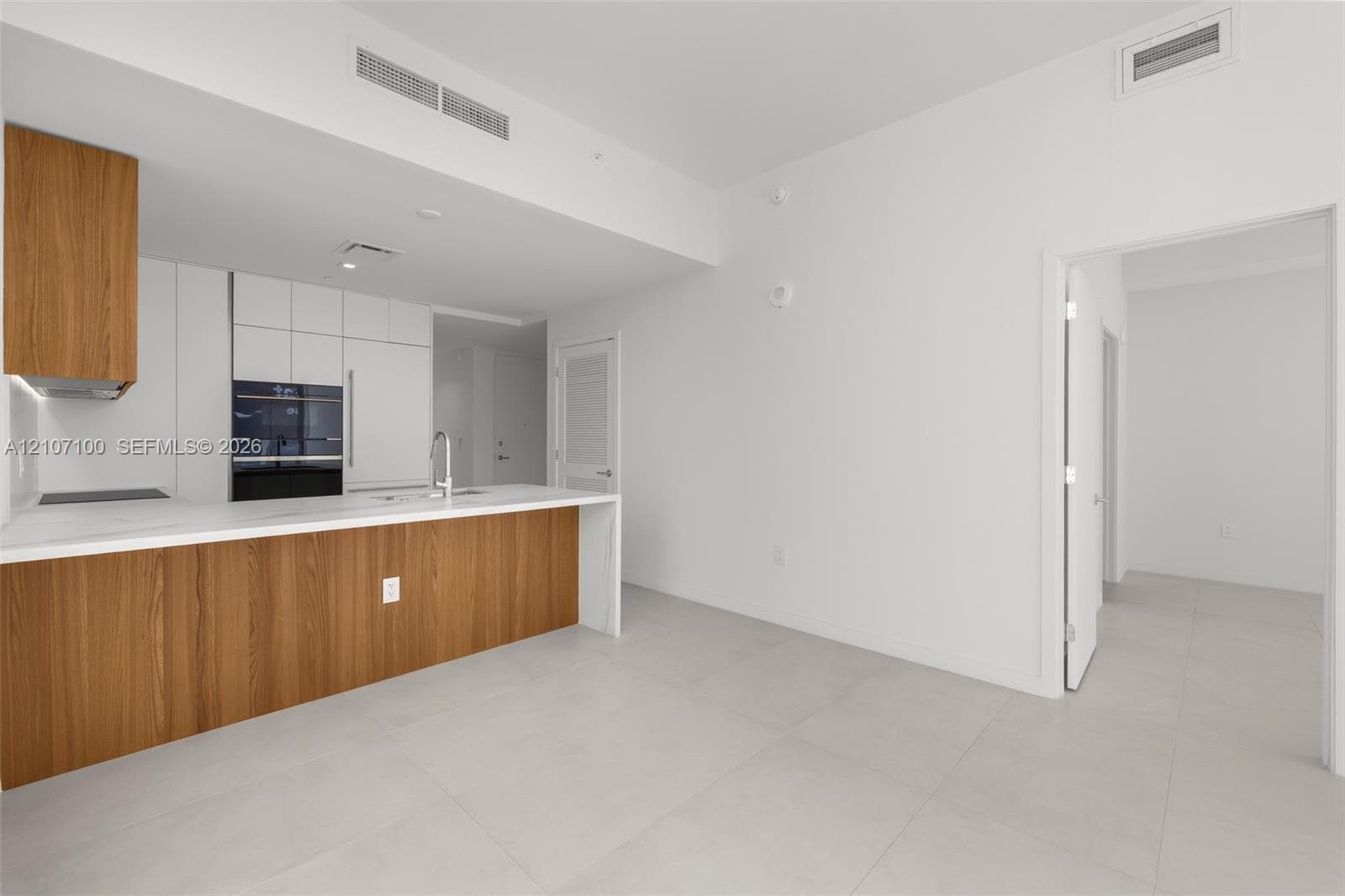 Floor-to-ceiling glass walls, expansive balcony access, neutral large-format tile flooring, and integrated white stone-finish countertop