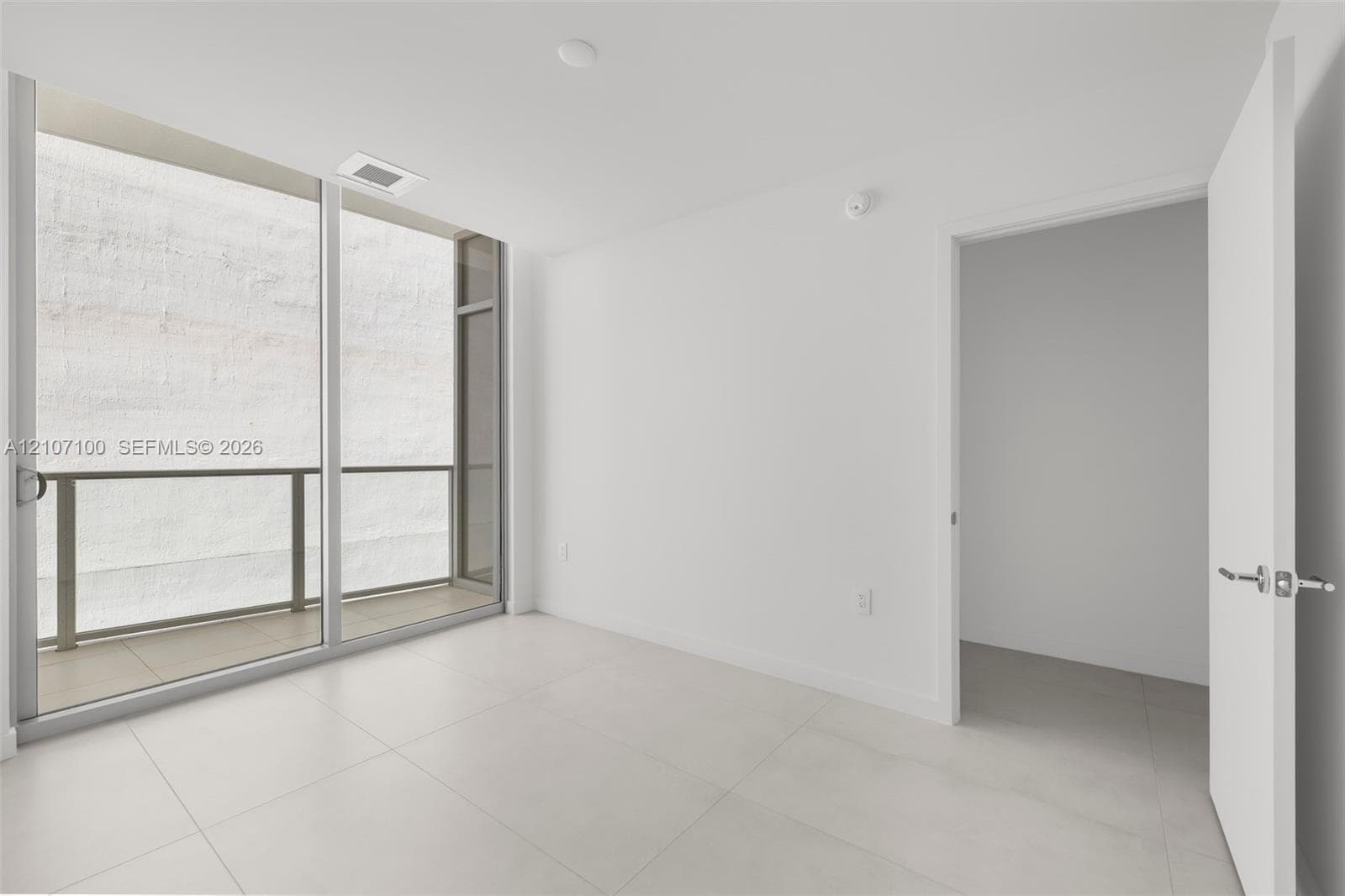Floor-to-ceiling sliding glass door, private balcony with metal railing, and large-format tile flooring
