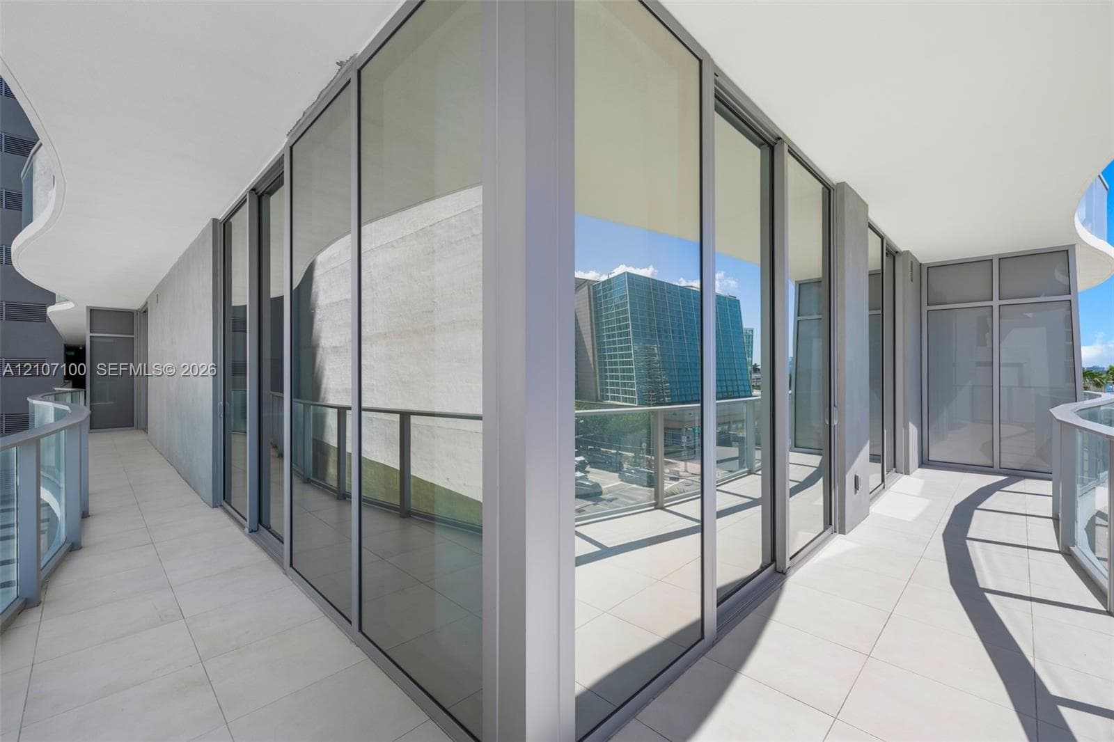 Wraparound balcony featuring large-format porcelain tile flooring, floor-to-ceiling glass panel walls, and metal railings