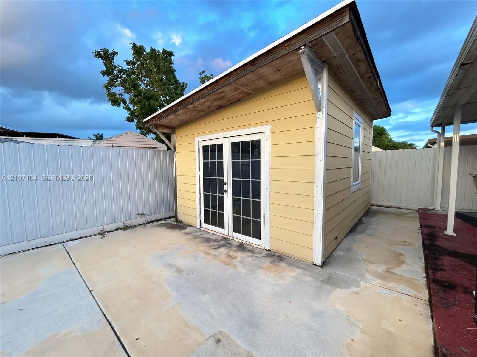 Detached structure featuring yellow horizontal lap siding, a single-slope roof, white-framed French doors with glass panes, and a concrete patio
