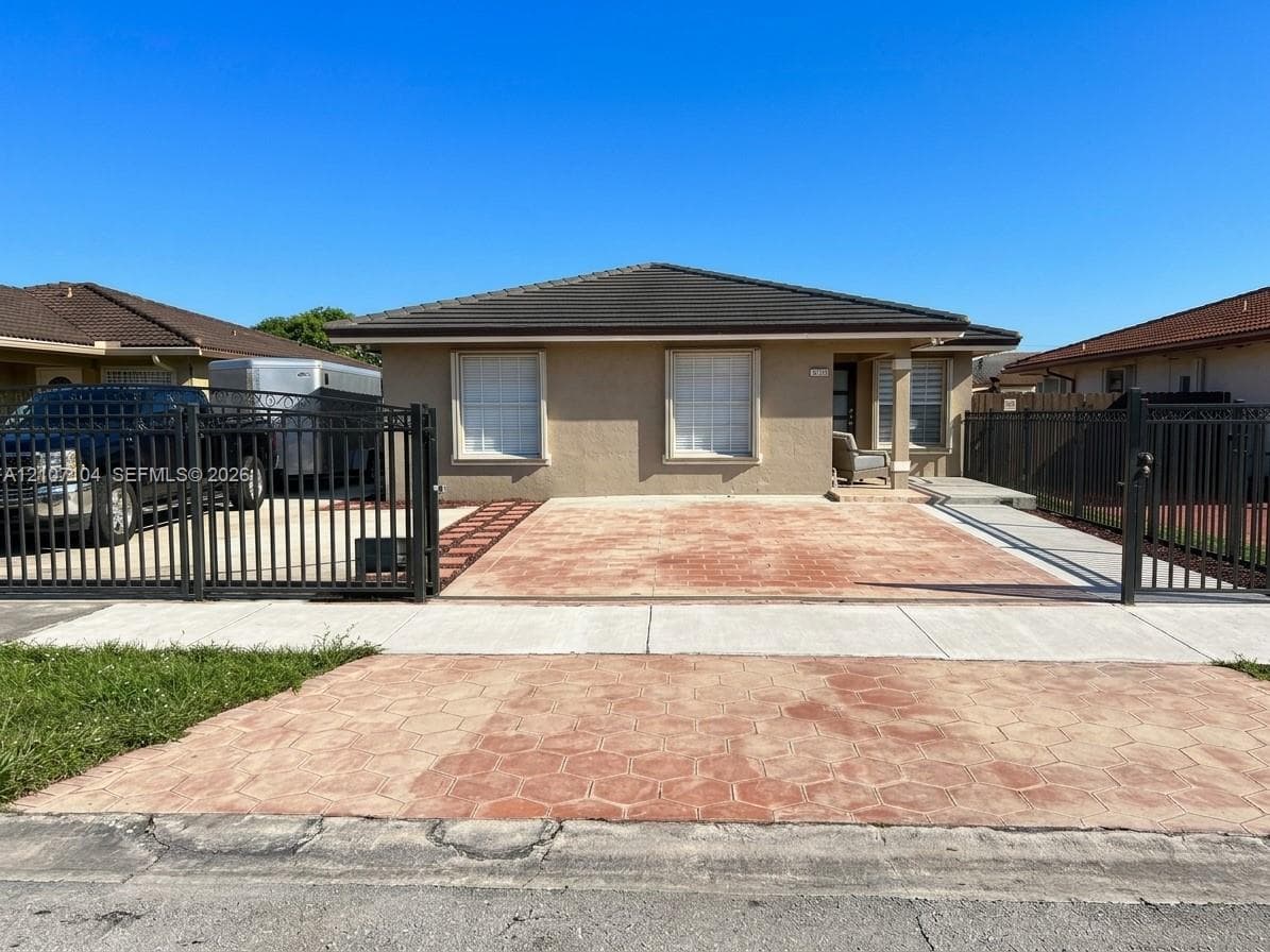 Single-story residence featuring a low-slope roof, stucco exterior, stamped concrete driveway, and a metal perimeter fence