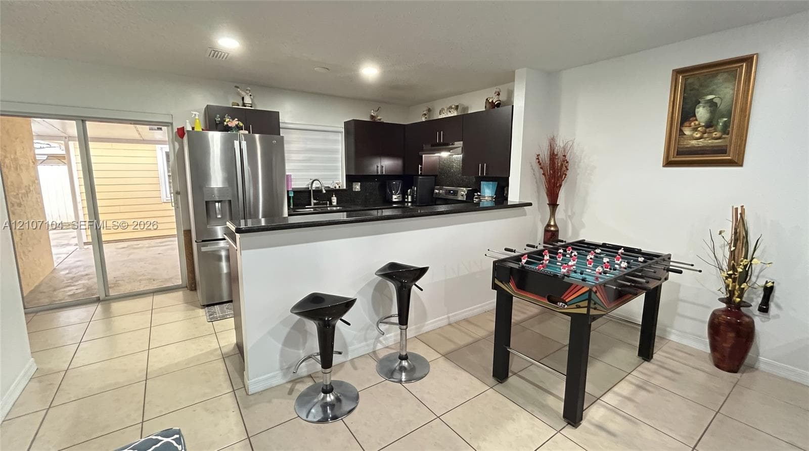 Kitchen featuring dark cabinetry, stainless steel refrigerator, stone-surface breakfast bar, recessed lighting, and ceramic tile flooring
