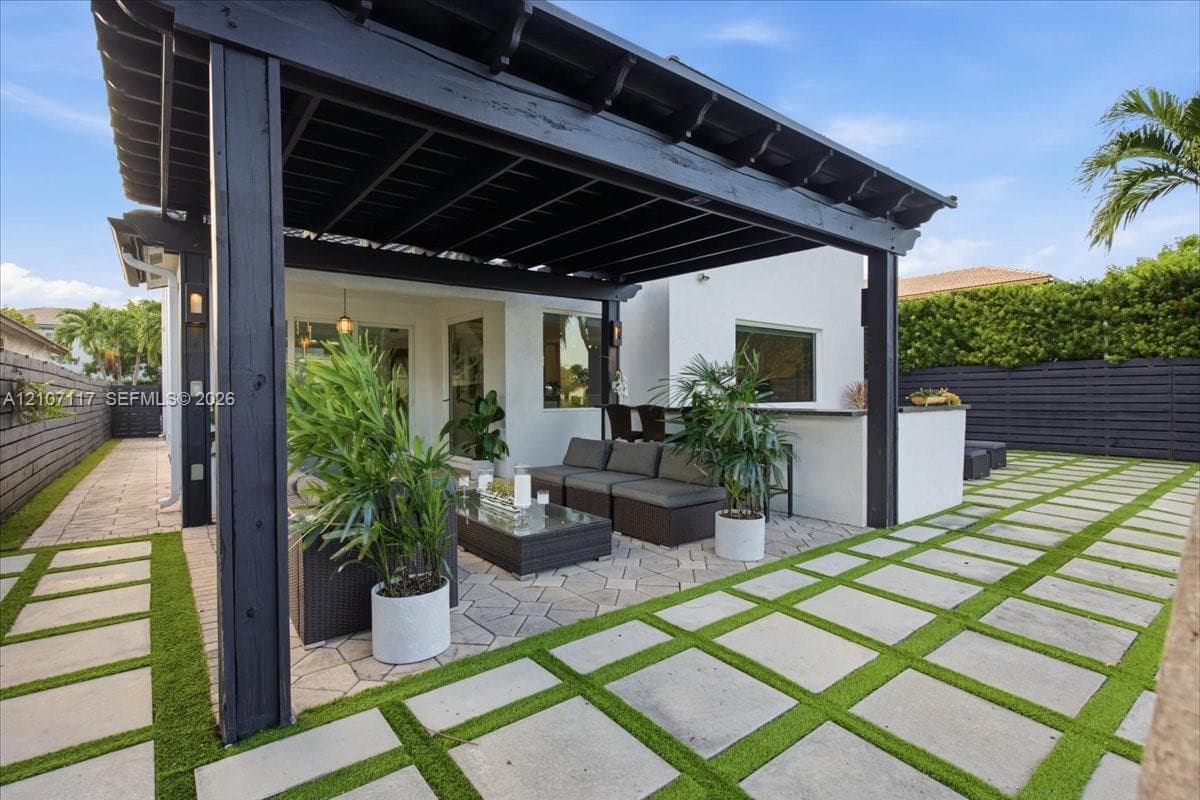 Outdoor patio featuring a black timber pergola, built-in stone counter, and stone paver flooring with synthetic turf inlays