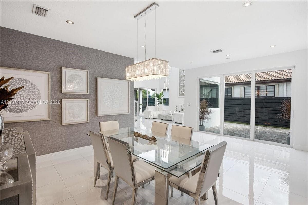 Dining area featuring large-format tile flooring, textured accent wall, rectangular tiered crystal chandelier, and oversized glass sliding doors